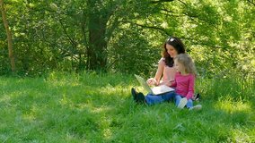 Family Spend Time Together Outdoors Using White Laptop. Two Girls are Playing Video Games Sitting on the Green Grass in the City Park.