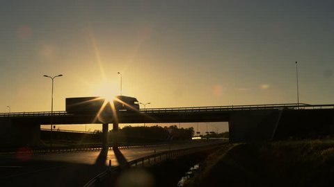 Side-View of a White Semi Truck with Cargo Trailer Driving Across a Bridge. Beautiful Scenery with Vehicle Moving on Overpass. It's Getting Dark and Sun is Setting. Shot on RED EPIC-W 8K Helium Camera