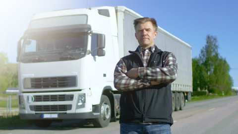 Professional Driver Gets out of the Parked White Semi Truck with Cargo Trailer Attached. Driver Stands in the Middle of the Road and Proudly Crosses Arms. Shot on RED EPIC-W 8K Helium Cinema Camera.