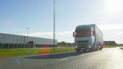 White Semi Truck with Cargo Trailer Attached Drives on the Empty Road. Industrial Warehouses by the Sides of the Highway and Sun Shines. Shot on RED EPIC-W 8K Helium Cinema Camera.