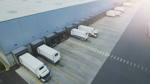 Moving Aerial Side Shot of Industrial Warehouse Loading Dock where Many Truck with Semi Trailers Load/ Unload Merchandise. Shot on Phantom 4K UHD Camera.