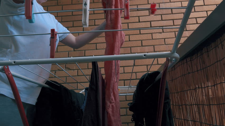 Woman hanging washed clothes on drying rack, female person doing laundry housework