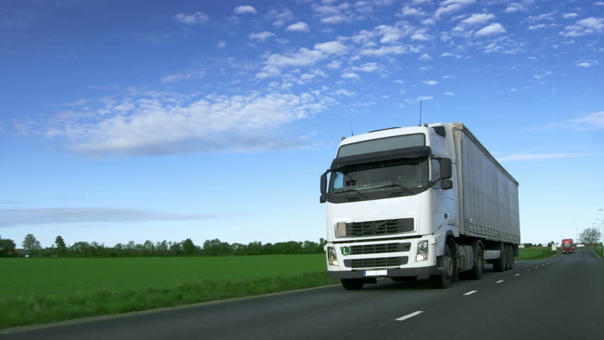 Speeding White Semi Truck with Cargo Trailer Drives on the Highway with Fields by the Sides of the Road. Shot on RED EPIC-W 8K Helium Cinema Camera. Royalty-Free Stock Footage #29800033