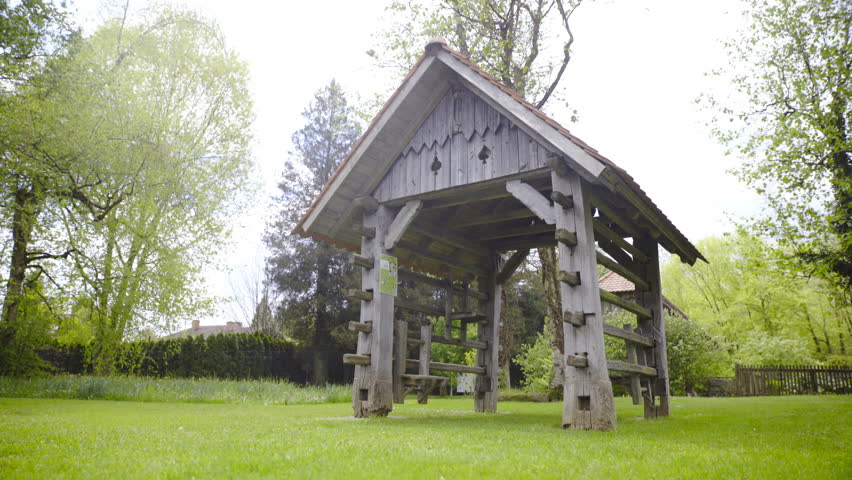 Slovenian hayrack miniature model on lawn 4K. Dolly slide show wide shot of wooden hayrack in focus under the bright sun and surrounded with forest.