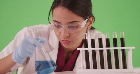 Young woman scientist chemist or medical researcher looking at blood samples in test tubes and beakers on greenscreen for compositing. Hispanic female student working on pharmaceutical research. 4k