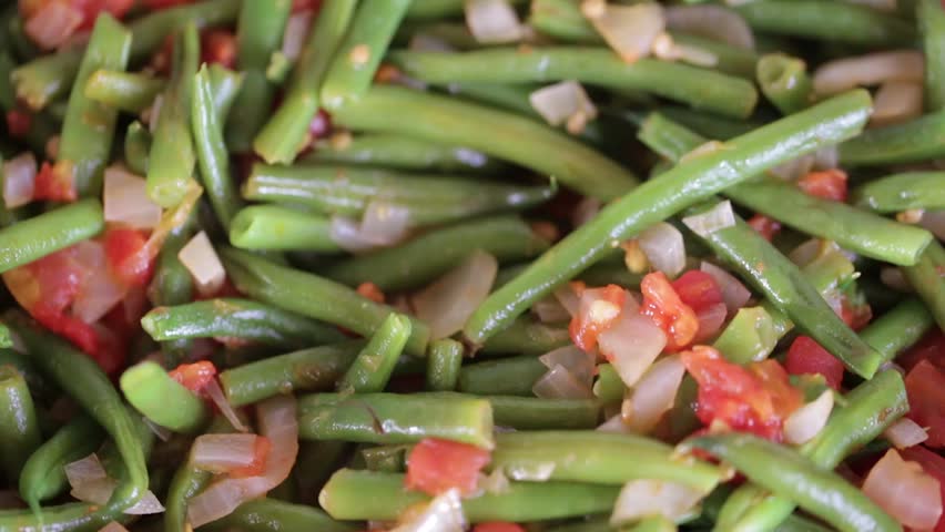 Chopped beans fried in a frying pan with tomatoes and onions