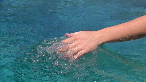 SLOW MOTION CLOSE UP: Detail of young woman dragging and sliding her hand through water surface splashing waterdrops and making waves in crystal clear sea. Girl playing with ocean water making circles