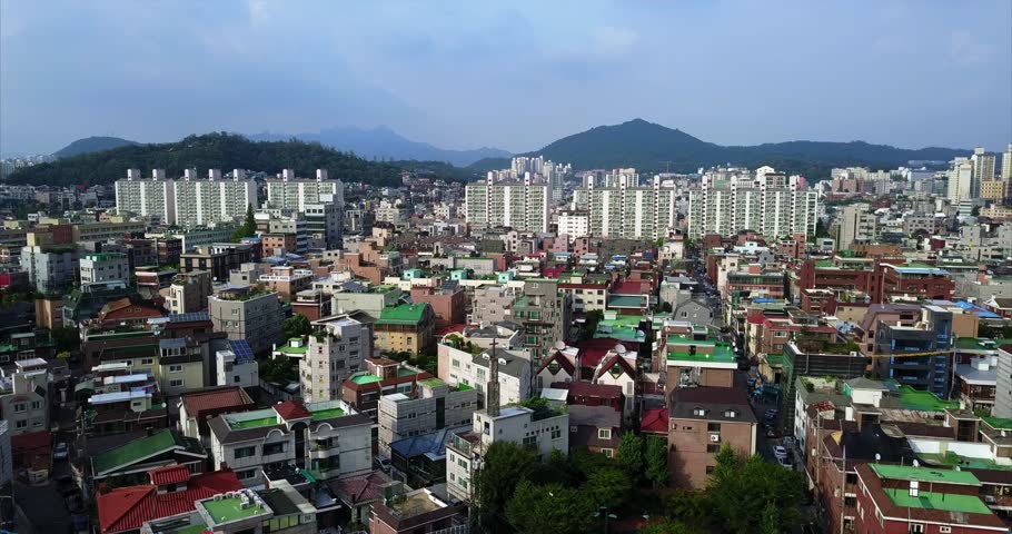 High aerial view over Hongdae’s colorful Seoul rooftops, streets, apartment towers, and distant mountains, 2017.