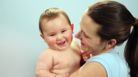Close-up of a mother holding a happy baby boy against a light blue wall
