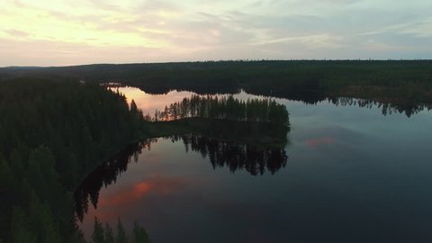 Aerial view of idyllic landscape with lake and forest at sunset. Flying over island and calm swamp lake in North Sweden