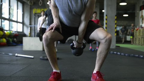 Young people in crossfit gym exercising, man lifting kettlebell