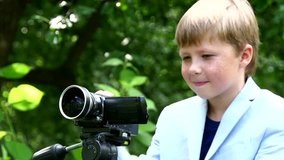 Young boy with video camera shoots movie about nature on green park slow motion. Kids outdoors in summer creative work of cinema. Beautiful footage. Itnteresting to look at world in childhood.