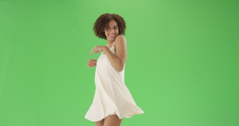 A young pretty African American woman twirls around in a sundress on green screen. On green screen to be keyed or composited.