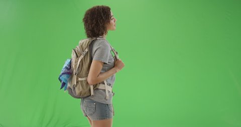 Young African American girl turns around looking cute and smiling at the camera on green screen. On green screen to be keyed or composited.