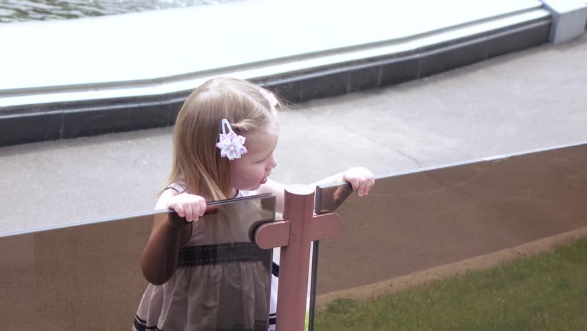 In the city park girl child through a glass railing looking at the fountain
