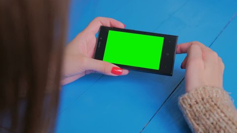 Woman using horizontal smartphone with green screen. Close up shot of woman's hands with mobile. Technology, chroma and internet concept