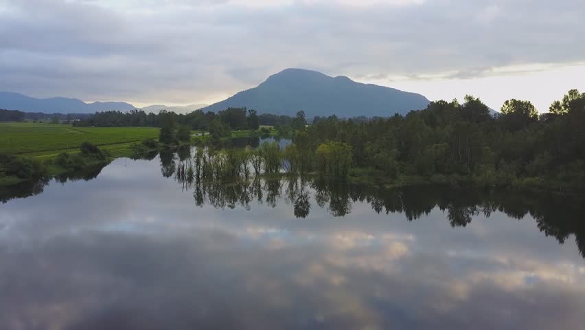 Aerial view of a beautiful lake, Nicomen Slough, with trees and a reflection of the cloudy sky above. Taken near Mission, East of Greater Vancouver, British Columbia, Canada.
