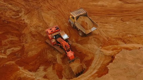 Aerial view mining excavator loading dumper truck. Heavy machinery working at sand mine. Crawler excavator pouring sand at mining truck. Mining machinery working in sand pit