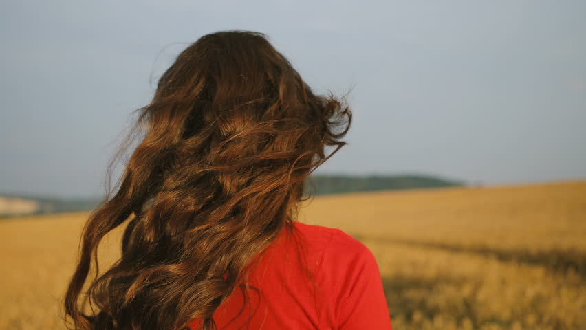 Portrait of beatiful young woman in stylish red dress walking in the golden field during the sunrise.