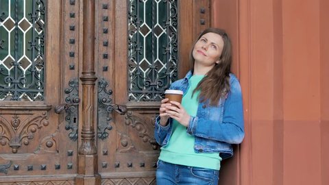Pretty girl in a cotton jacket drinking coffee. Vintage building in the background.