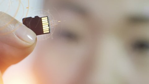 Closeup of Asian woman holding micro SD card with computer animated equalizers and data around it. Technological background