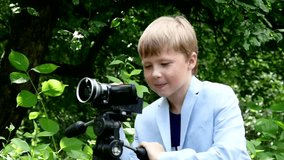 Young boy looks into video shoots movie about nature on green park slow motion. Kids outdoors in summer are creative work of cinema. Beautiful footage for family. Interesting world in childhood.