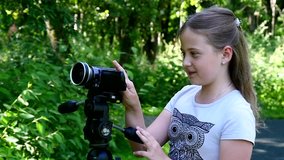 Young girl looks into video camera on background of green park slow motion. Children outdoors in summer are creative work of cinema. Beautiful footage for family. Interesting world in childhood.
