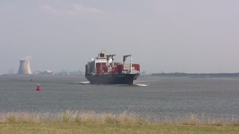 BATH, NETHERLANDS - JUNE 2017: Container ship Cap Beatrice navigates on the Western Scheldt, in The Bocht van Bath (the curve of Bath). Cooling towers of the nuclear power plant Doel in background.