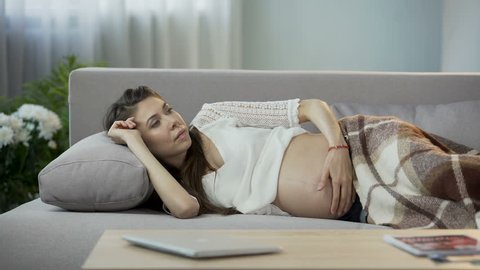 Pregnant lady lying on sofa, having sudden vomiting urge, breathing to calm down