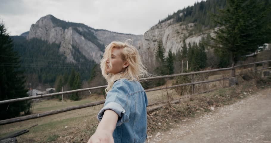 She looks incredibly beautiful. The edge of the mountains. Follow me. Young attractive woman carries her partner's hand, leading him on a sunset.