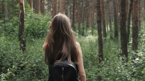 On a sunny day, a portrait of a beautiful young tourist girl, with a backpack, fashion woman, walks through the forest, the background of trees. Concept: recreation, beautiful view, sports, travel. Stock Video
