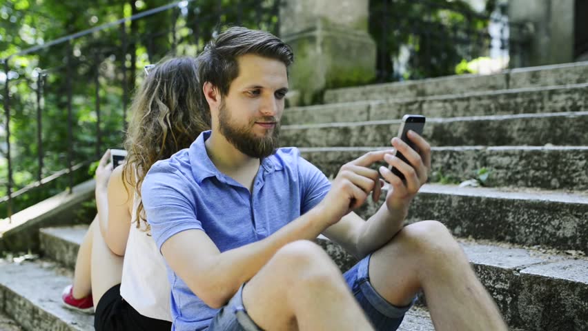 Young couple with smartphones sitting on stairs in town.