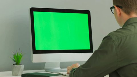 Close up shot of young man in the glasses using computer with green screen at the modern office table. Chroma key.