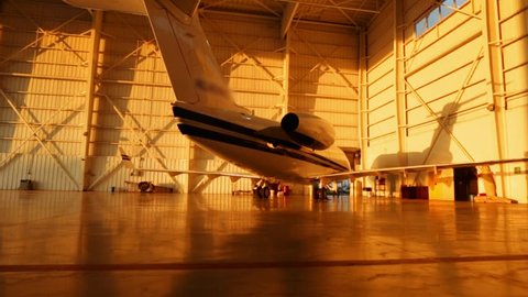 Beautiful pan of private jets parked in aircraft hangar and outside during Sunset