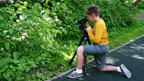 Young boy with video camera shoots film in nature of green park slow motion. Children outdoors in summer are creative work of cinema. Beautiful footage for family. Interesting world in childhood.