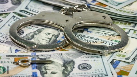 Pair of handcuffs closeup on dollar banknotes background. Corruption problem
