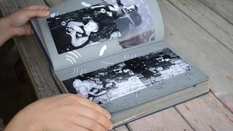 Girl leafing through a photo album with old photos which lies on the table close-up