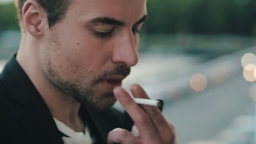 Handsome man takes a cigarette and light it up. Young man smokes a cigarette against backdrop evening city. Tired man smokes a cigarette on background evening lights city | Shutterstock HD Video #29868232
