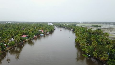 Aerial back view following a Boat Houses over the backwaters in Alleppey, Kerela with coconut trees on both sides in UHD 4K