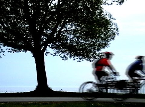 A group of cyclists ride along a beach boardwalk at dusk - moving from left to right.