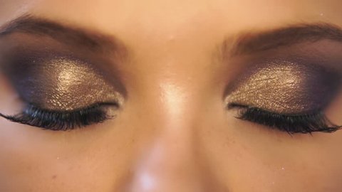 Closeup view of woman's eyes with beautiful golden makeup opening and closing in slowmotion