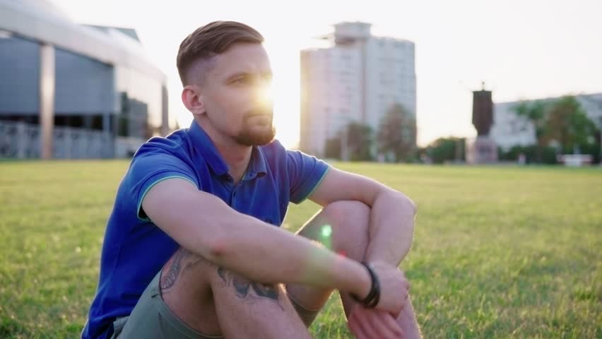Young hipster man sitting on grass in city park