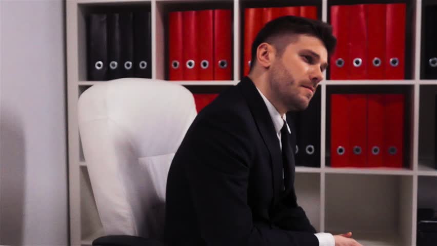 Portrait of successful businessman looking serious on camera at office. He turning on armchair near shelf with folders. Super slow motion rapidly shot.