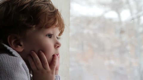 Boy looking out the window at the falling snow, videoclip de stoc