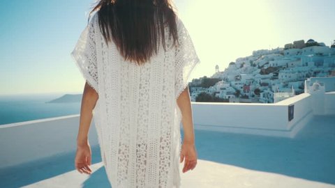 Young sexy woman is on the greek island Santorini in a white dress and and straw hat white greek houses volcano sea sunny weather
