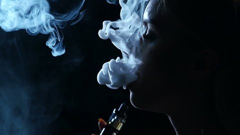 Girl smokes an electronic cigarette. Black background. Close up. Silhouette. Slow motion