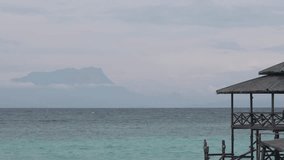 Video footage of Kinabalu mountain with beautiful turquoise color ocean and a wooden jetty at the foregound
