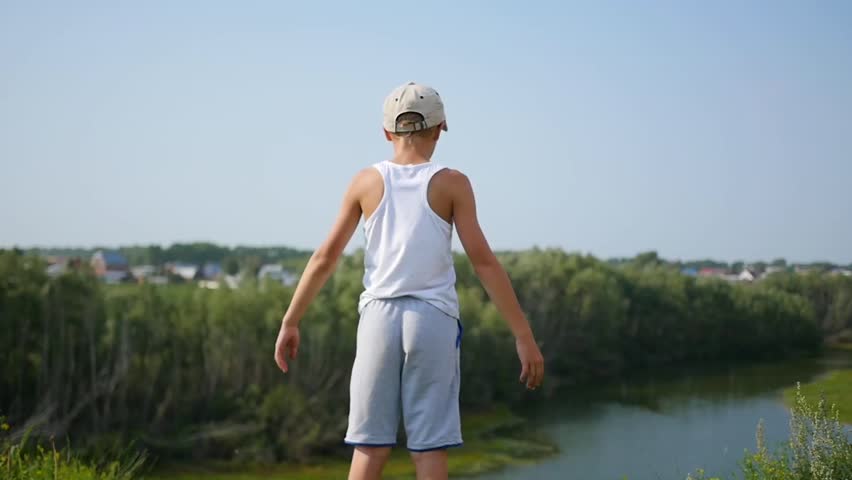 A young guy is standing on the river bank. Beautiful summer landscape