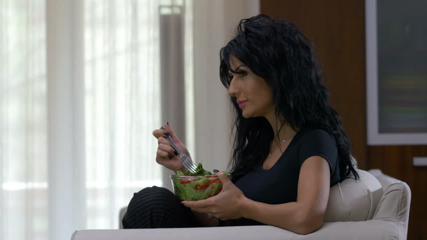 Attractive woman eating a bowl of lettuce and tomatoes vegetable salad dish watching tv at home | Shutterstock HD Video #29921851