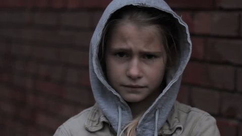 Refugee homeless child. Dark portrait of preteen girl standing in front of brick wall, she is looking unhappy and angry.